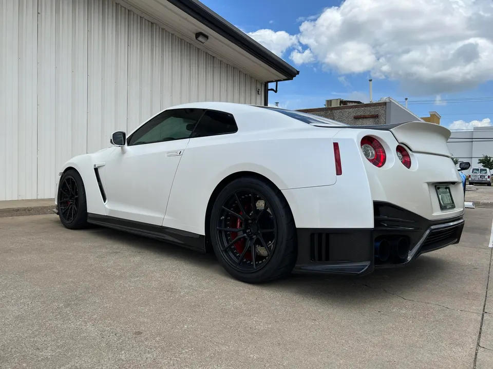 White Nissan GT-R R35 with aftermarket black wheels, carbon fiber side skirts, and rear diffuser parked outside.