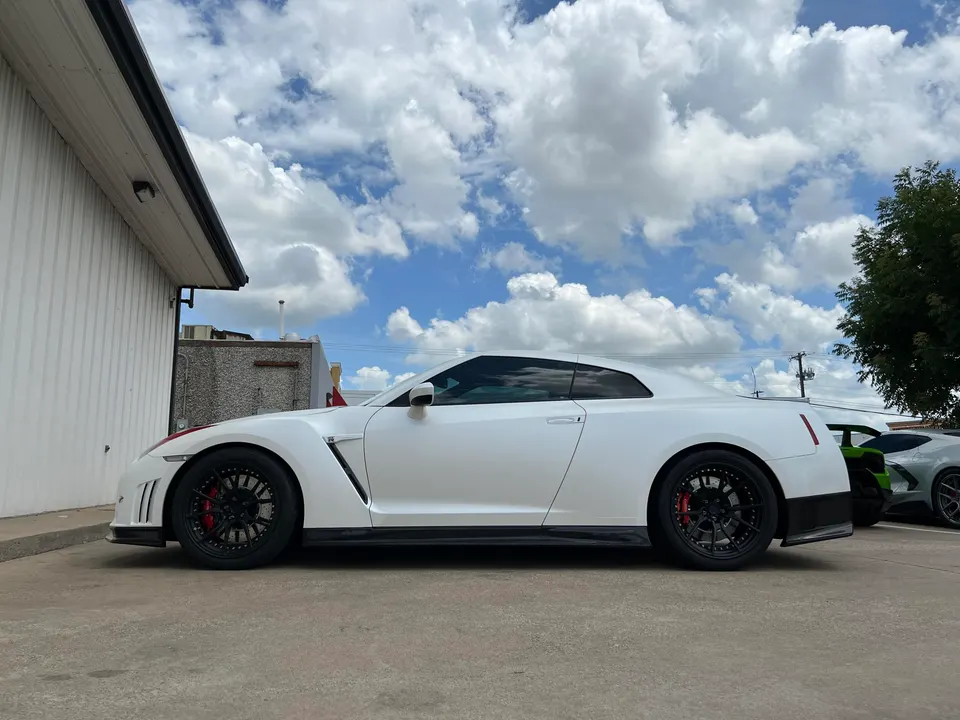 White Nissan GT-R with black aftermarket wheels and red brake calipers parked outdoors on a sunny day.