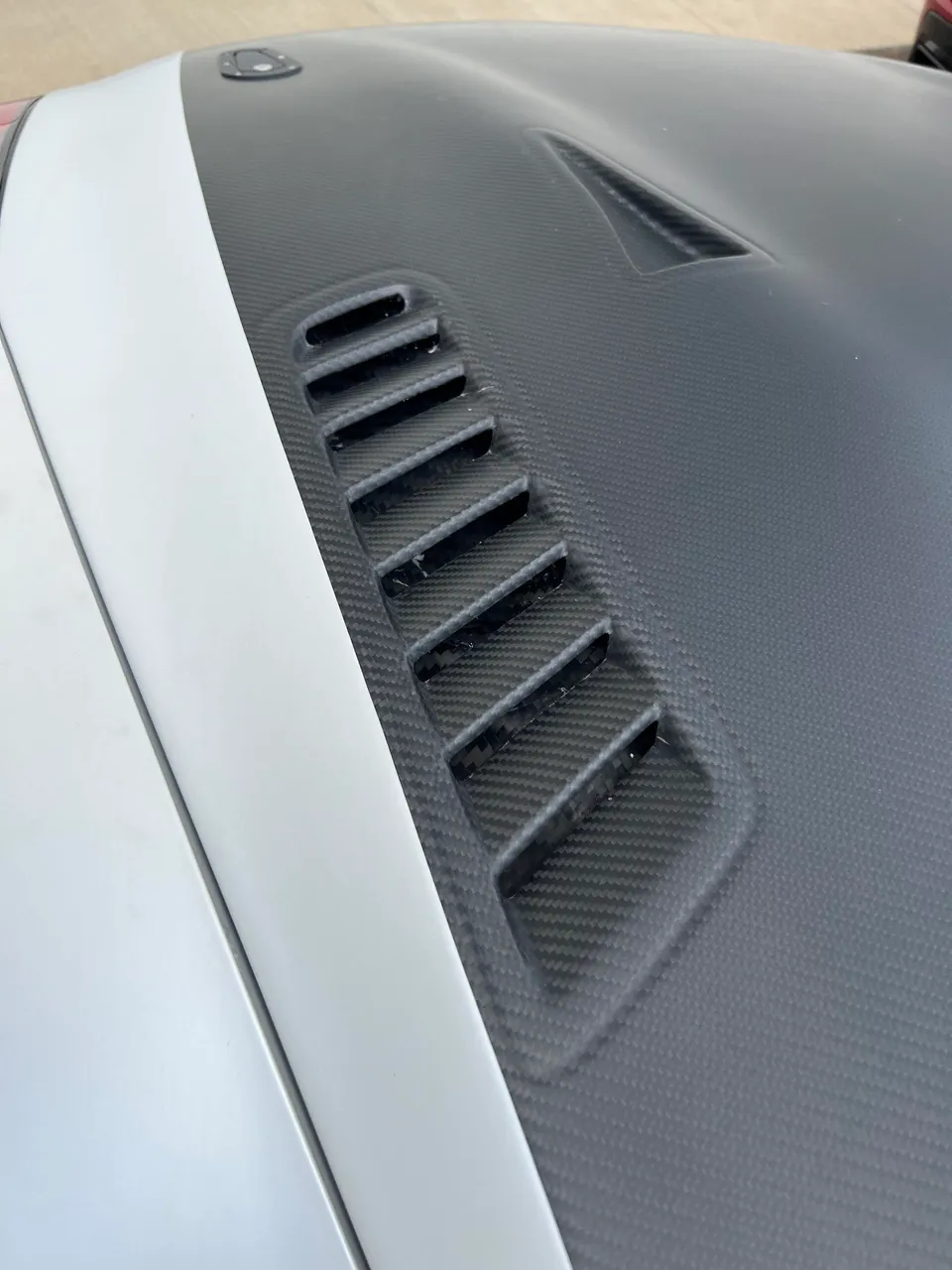 A close-up of a white car's carbon fiber hood with functional vents.