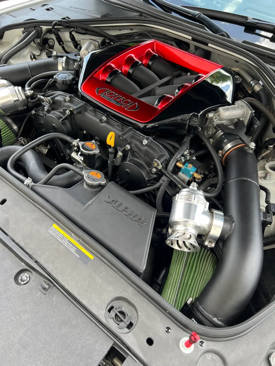 A detailed shot of a Jotech tuned Nissan GT-R engine bay with a red intake manifold, aftermarket air filters, and blow-off valve.
