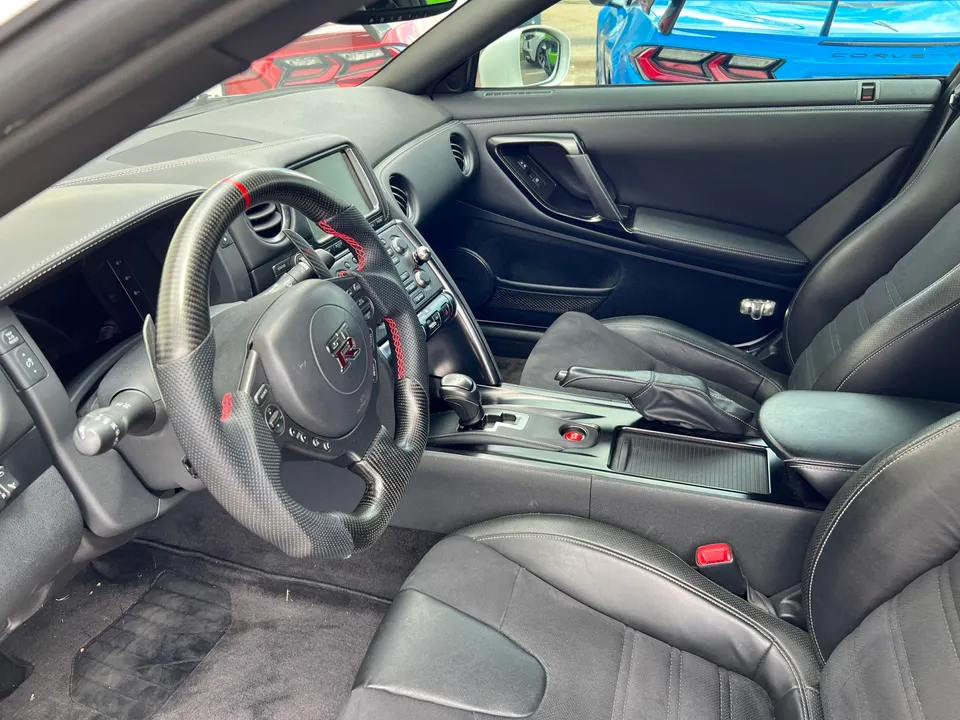 Interior view of a Nissan GT-R featuring a carbon fiber steering wheel, black leather seats, and center console.