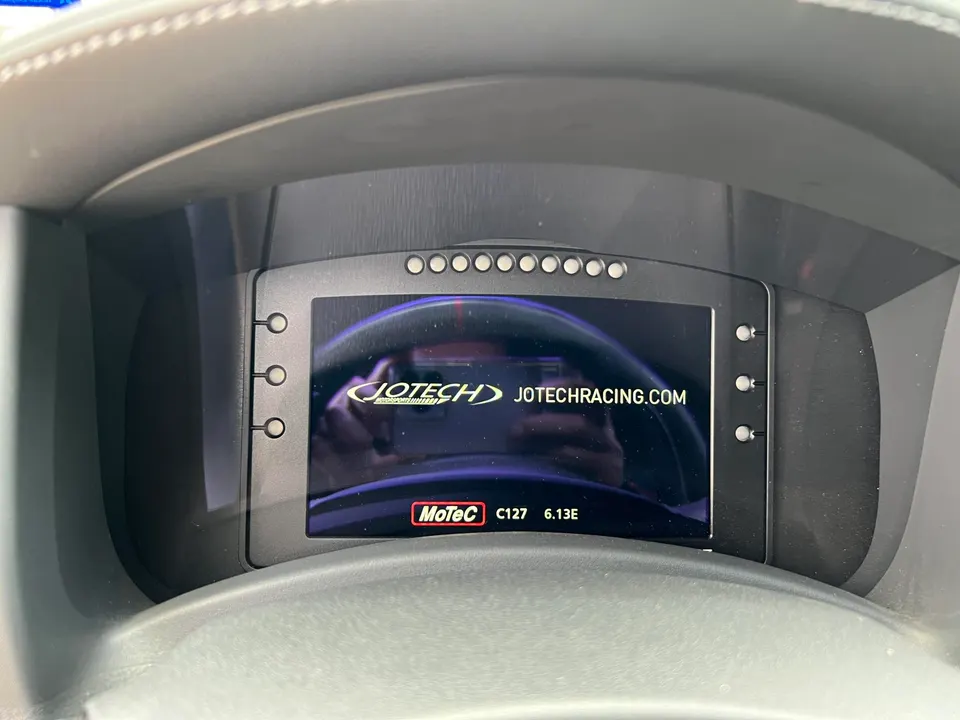 Close-up of a MoTeC C127 digital dash displaying Jotech Racing branding in a performance car interior.