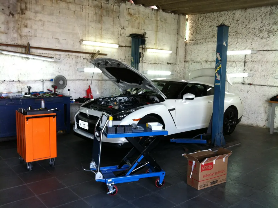 A white Nissan GT-R with its hood open, undergoing maintenance in a garage with tools and a car lift.
