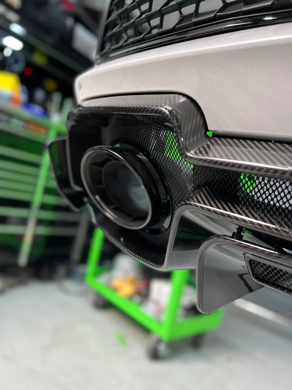 Close-up of a performance car's carbon fiber rear diffuser and exhaust tip in a shop setting.