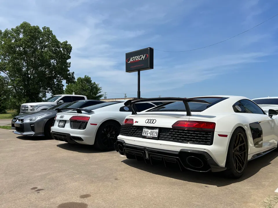 Multiple high-performance sports cars, including Audi R8s and a Nissan GT-R, parked outside Jotech Motorsports.