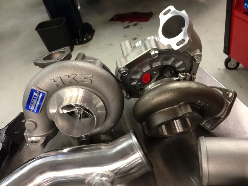 Two HKS turbochargers and boost piping on a workbench in a performance tuning shop