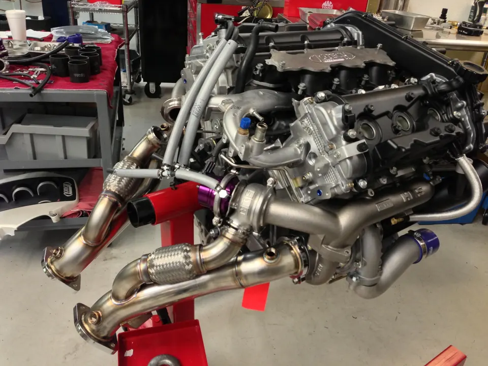 High-performance engine with twin turbochargers and custom exhaust manifolds on an engine stand in a tuning shop.