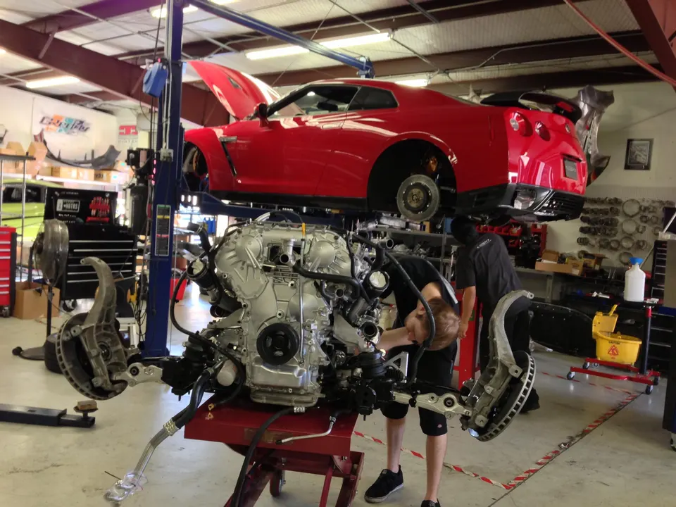 Red Nissan GT-R on a lift in a performance shop with its engine and front subframe removed for service.