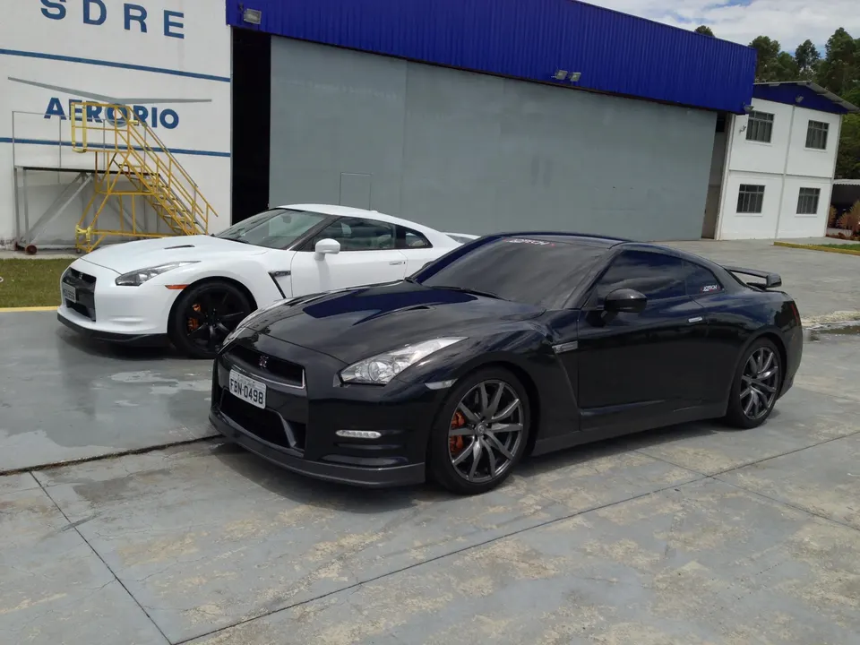 Two Nissan GT-R R35s, one white and one black, parked side-by-side outside an industrial building.