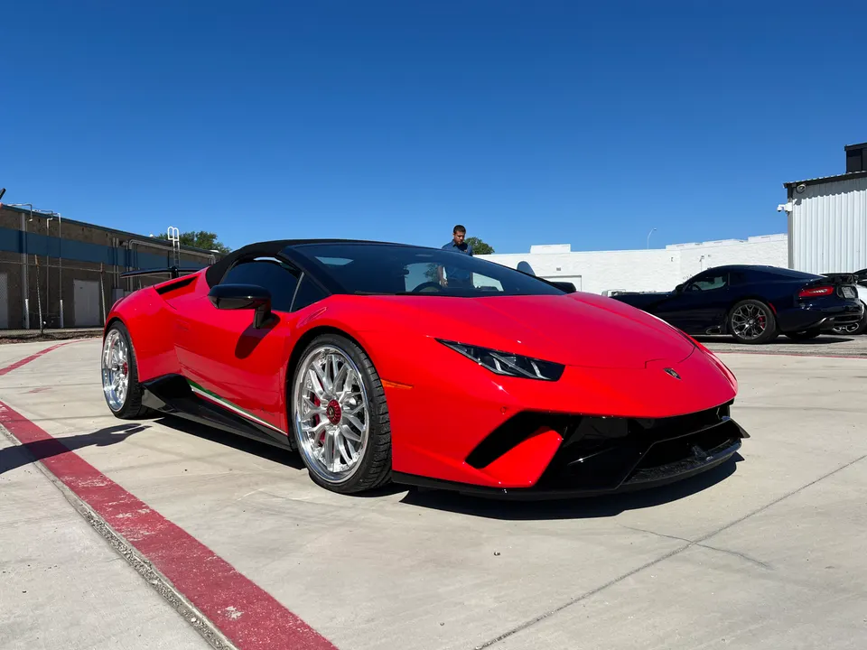 A red Lamborghini Huracan convertible with custom wheels parked outdoors on a sunny day.