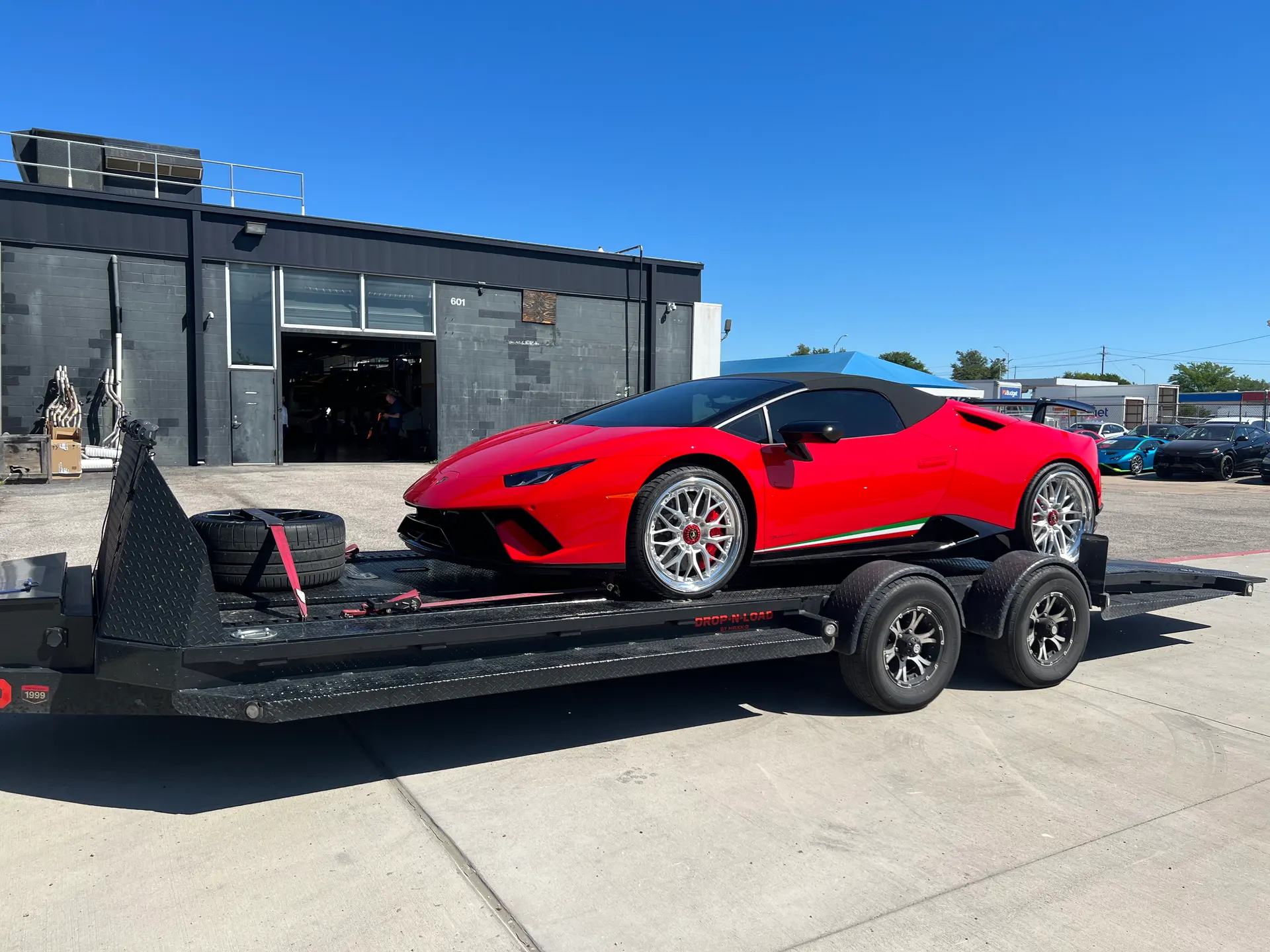 Red Lamborghini Huracan convertible on a car trailer outside a performance tuning shop on a sunny day