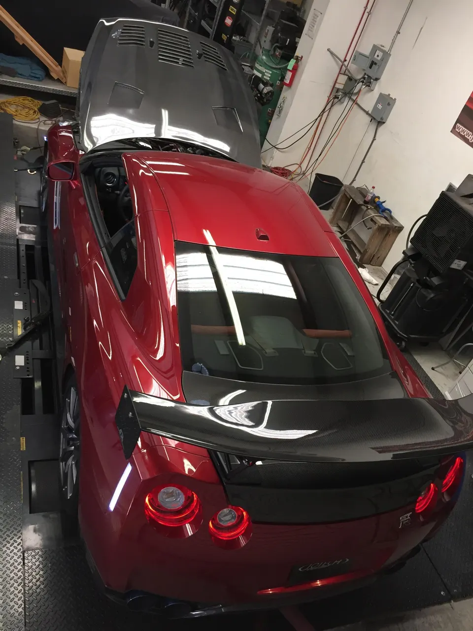 A red Nissan GT-R with a carbon fiber hood and wing strapped to a dynamometer at Jotech Motorsports.