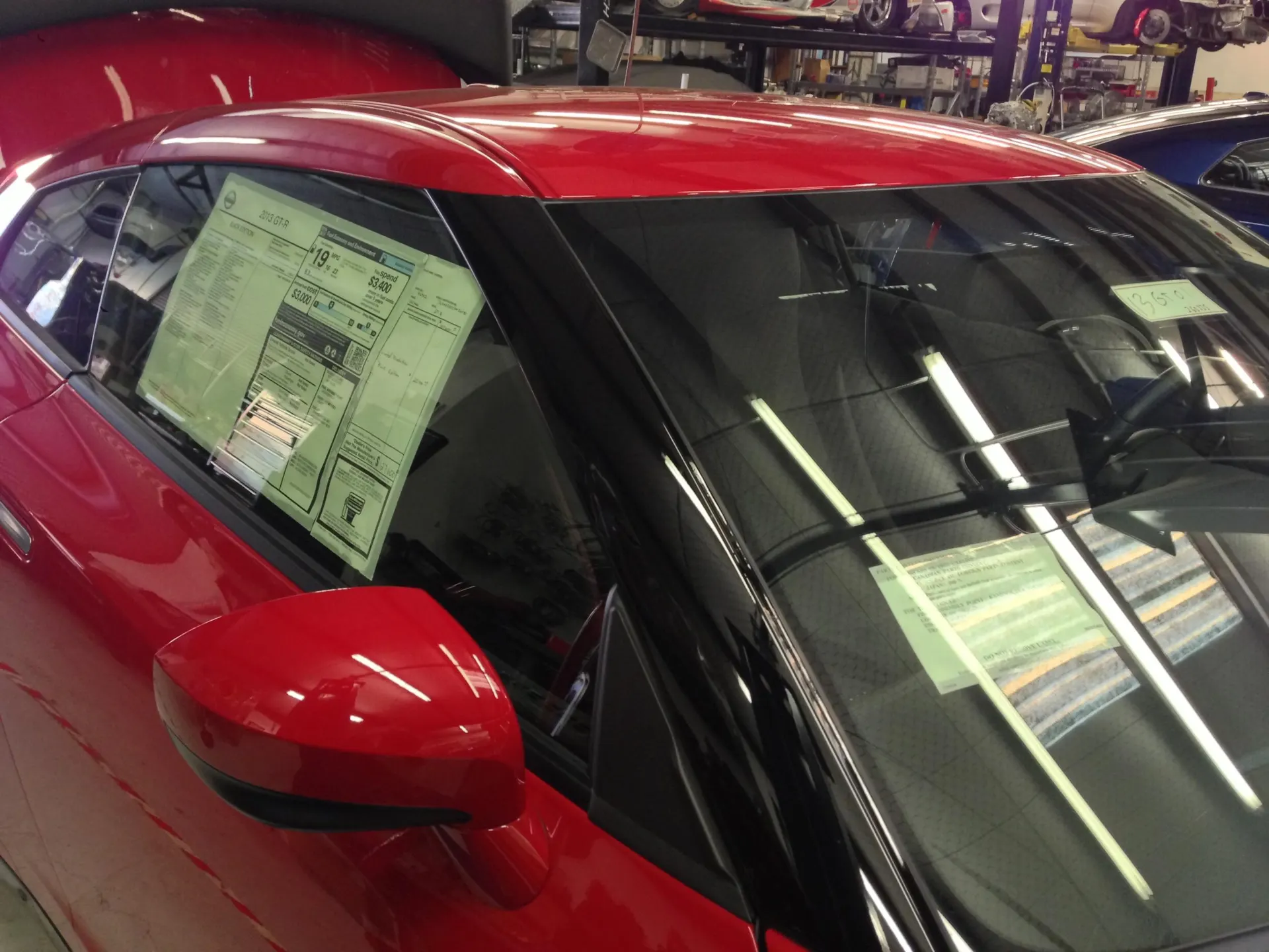 A red Nissan GT-R with a window sticker visible on the side window, parked inside a shop or dealership.