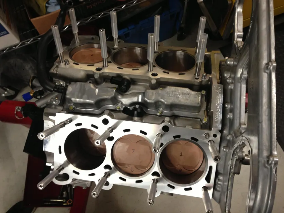 A close-up of a VR38 engine block with pistons and head studs during assembly in a performance shop.
