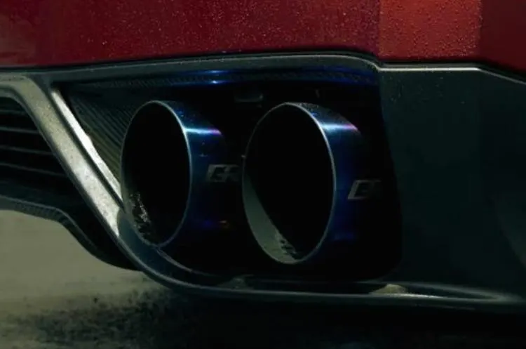 Close-up of blue titanium GReddy exhaust tips on a red performance car's rear bumper.
