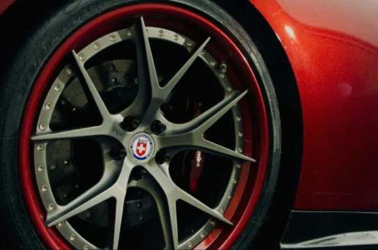 Close-up of a custom car wheel with a red lip, multi-spoke design, and performance brakes.