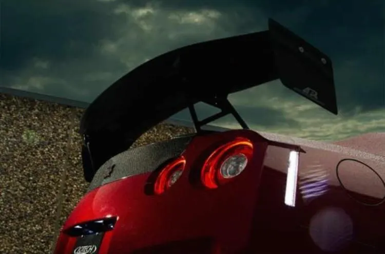 Rear view of a red Nissan GT-R with a large carbon fiber aftermarket wing and custom taillights against a dramatic sky.