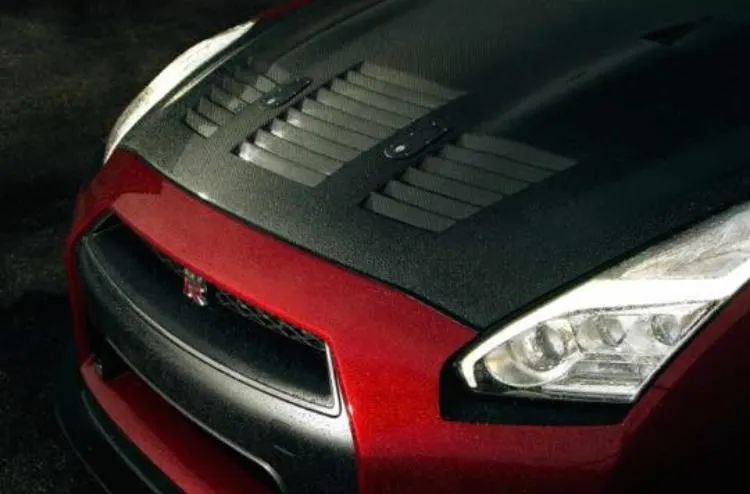 Close-up of a red Nissan GT-R's front end, showcasing a carbon fiber hood with integrated vents.