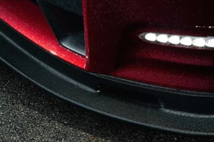 Close-up of a red car's front bumper and carbon fiber splitter with LED daytime running lights.