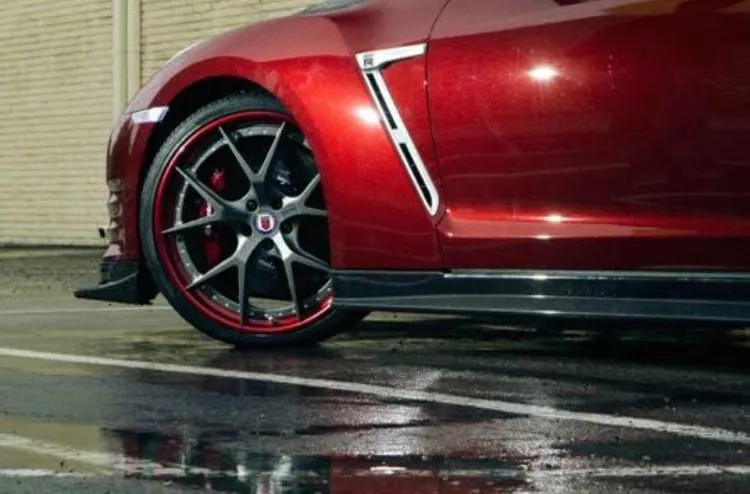 Red Nissan GT-R with custom multi-spoke wheels and red accents parked on a wet surface, showcasing the side profile.