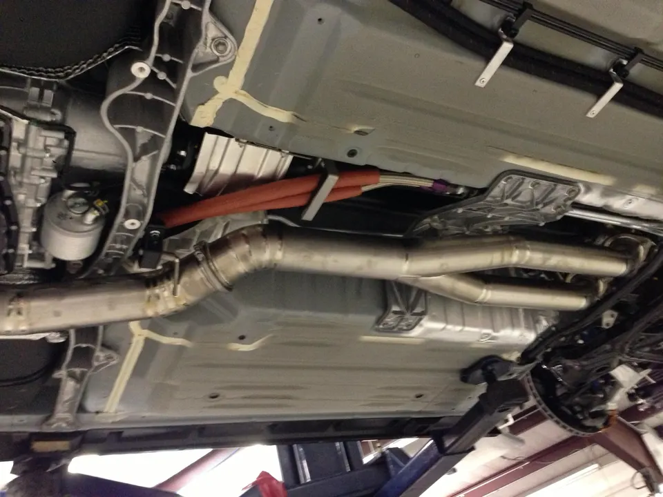 Underside view of a performance car on a lift, showcasing the aftermarket exhaust system, drivetrain, and fuel lines.