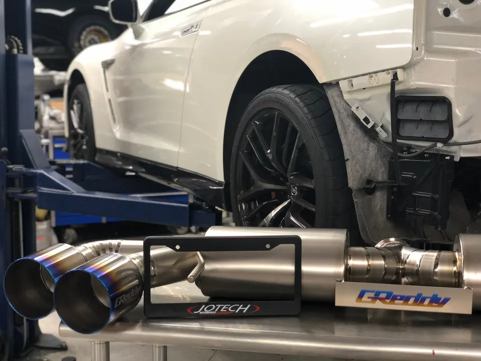 White Nissan GT-R on a lift in a Jotech Motorsports shop with a GReddy exhaust system on a table, ready for install.