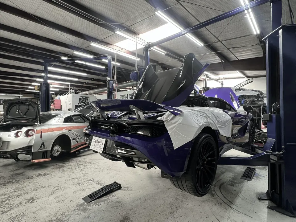 A purple McLaren on a lift with its doors open and a silver Nissan GT-R with its trunk open in a performance tuning shop.