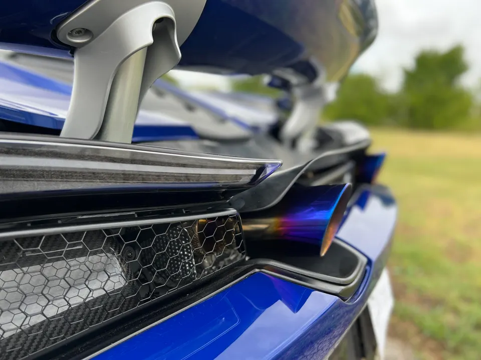 Close-up of a blue supercar's rear, showcasing the iridescent exhaust tip and carbon fiber grille.