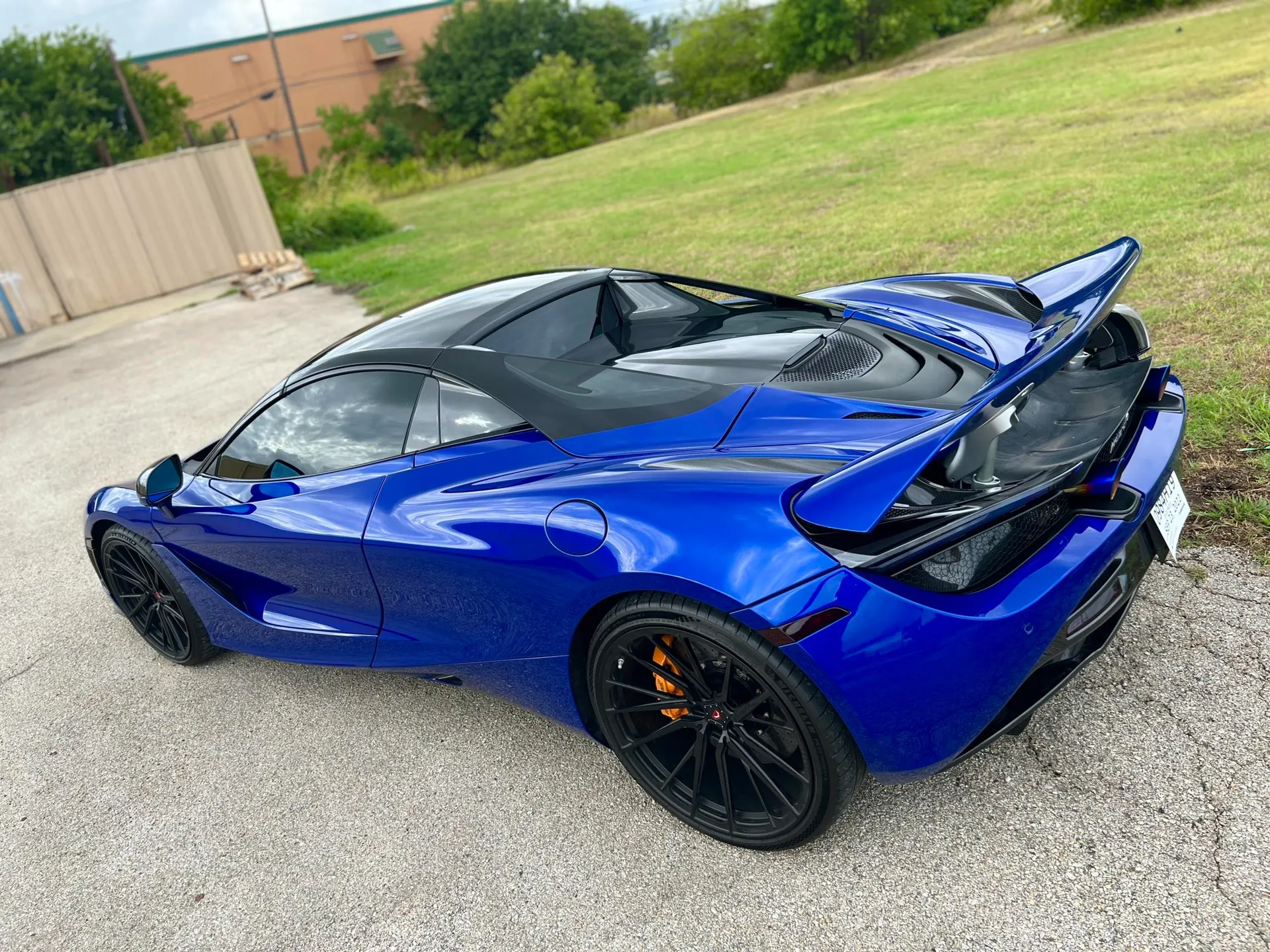 Blue McLaren 720S supercar with aftermarket black wheels and a prominent rear wing parked outdoors.