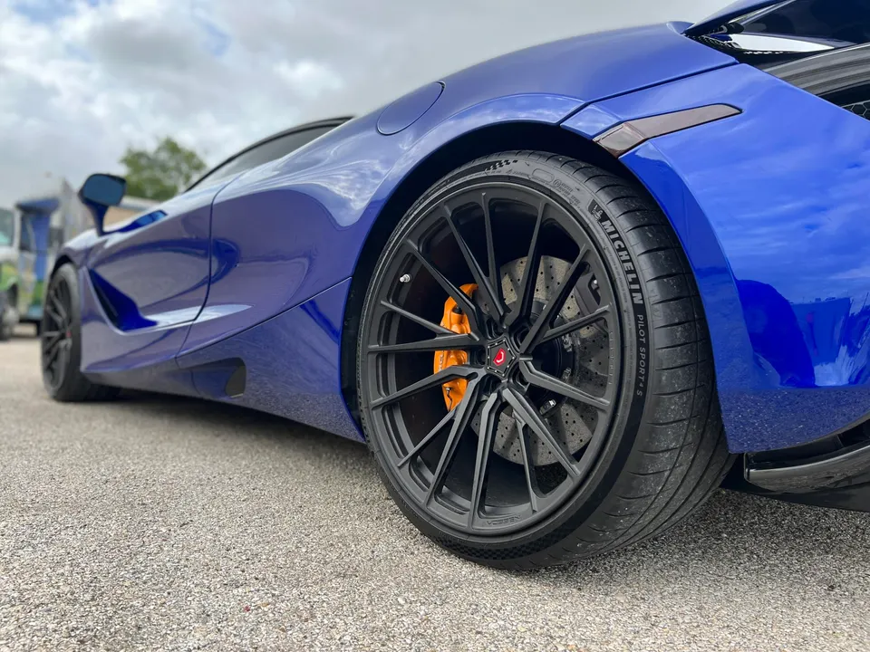Close-up of a blue McLaren's rear wheel, featuring black Vossen wheels, Michelin tires, and orange brake calipers.
