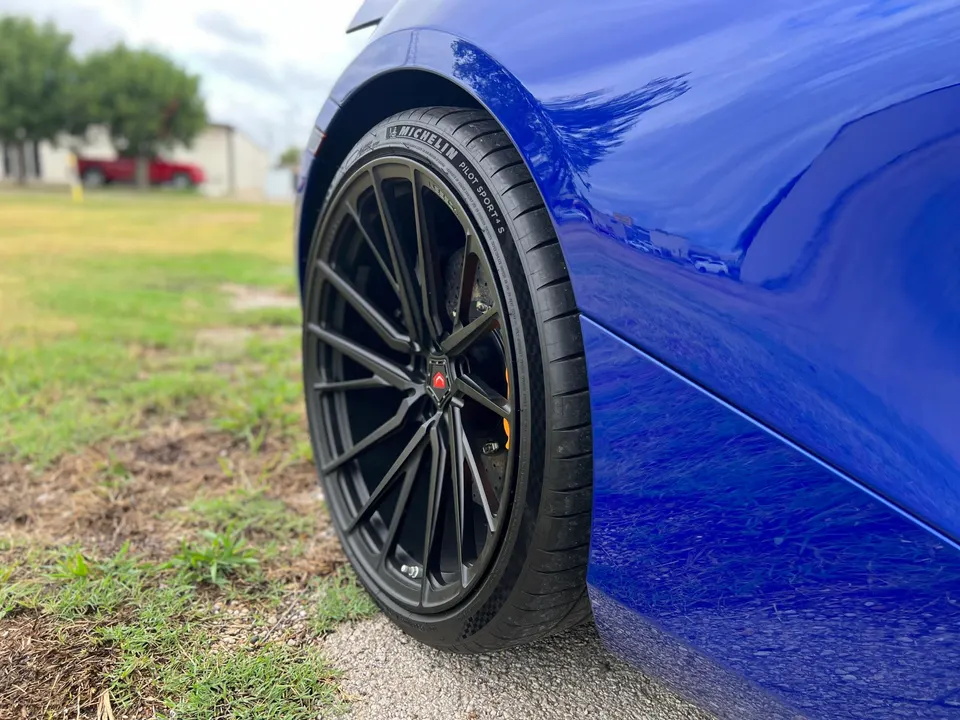 Close-up of a blue car's black multi-spoke custom wheel with Michelin Pilot Sport 4S tire and orange brake caliper.
