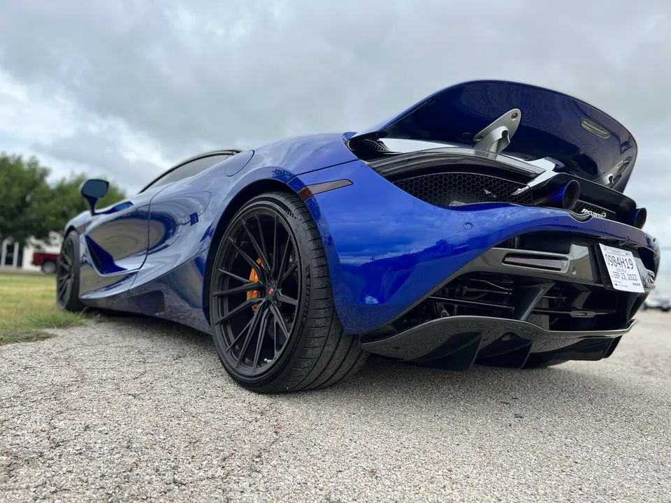 Blue McLaren 720S with aftermarket black wheels, active rear wing, and custom exhaust tips parked outdoors.