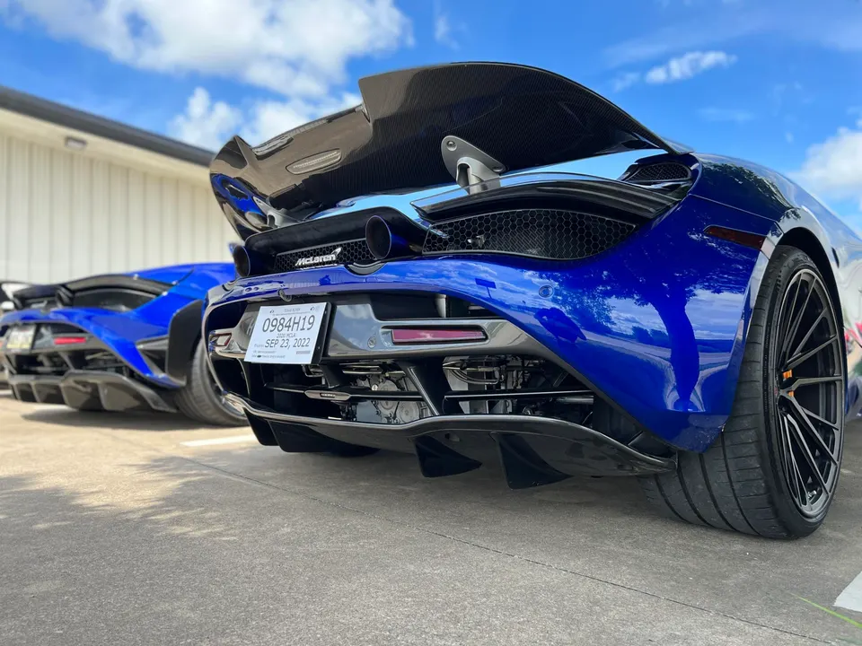 Two blue McLarens, one a 720S, parked outdoors showcasing their carbon fiber rear wings and aggressive diffusers.