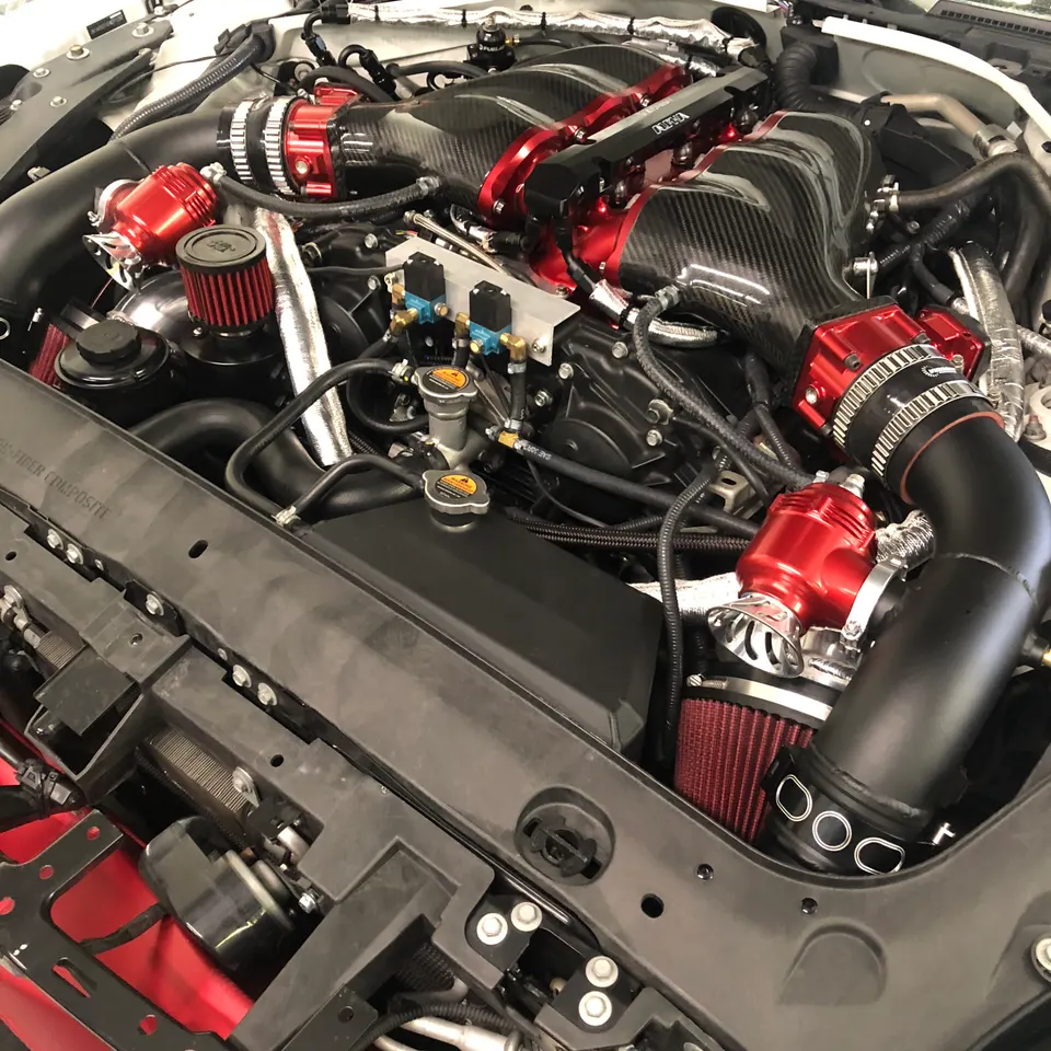 Close-up of a highly modified engine bay featuring a carbon fiber intake manifold, red air filters, and blow-off valves.