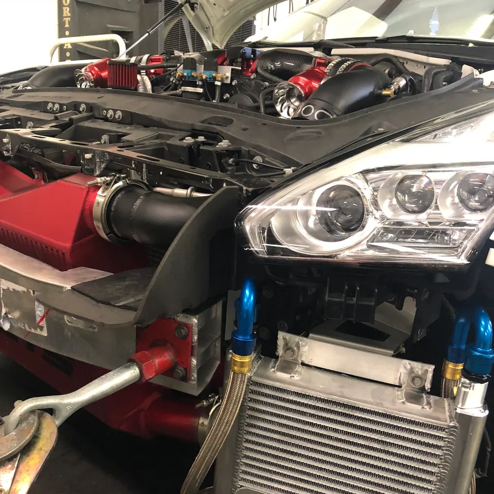 Front view of a Nissan GT-R in a shop with the bumper removed, showcasing a large red intercooler and performance intake system.