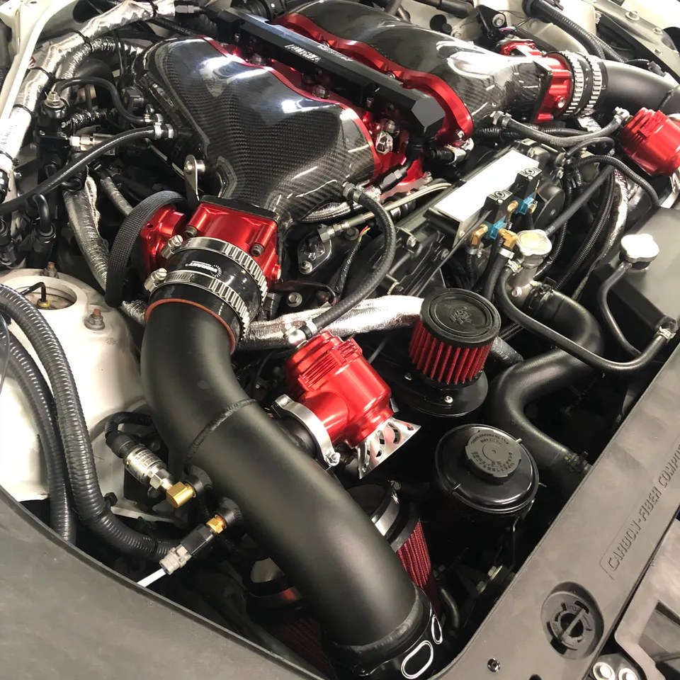 Highly modified engine bay featuring a carbon fiber intake manifold, red air filters, and performance boost components.