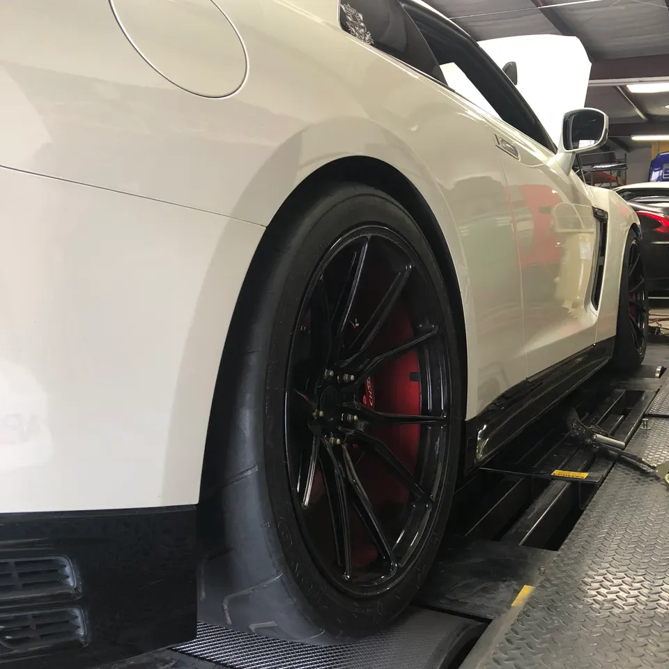 White Nissan GT-R on a dyno showing black aftermarket wheels with red brake calipers and performance tires
