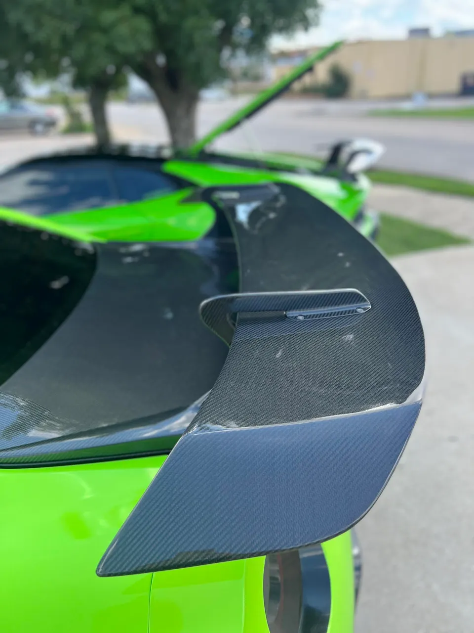 Close-up of a bright green sports car's carbon fiber rear wing.