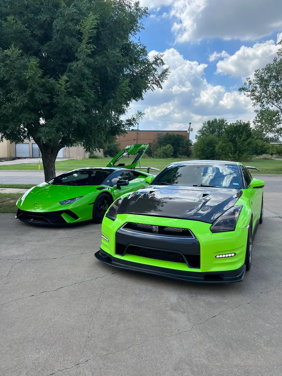 A bright green Nissan GT-R and a matching Lamborghini Huracan parked outdoors on a sunny day.