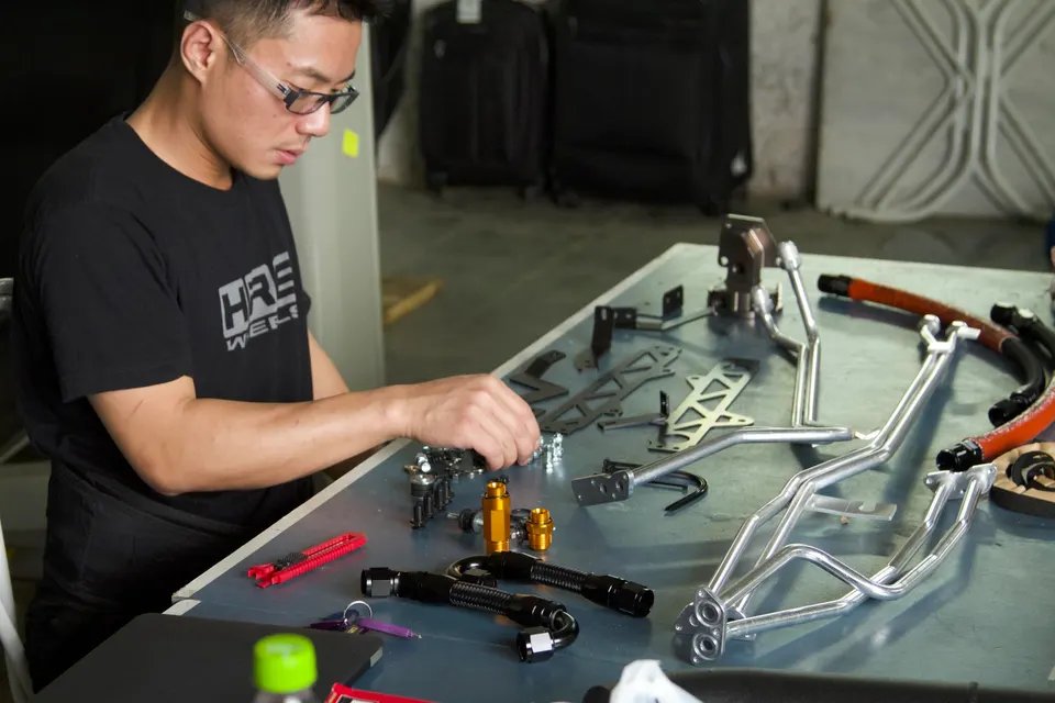 A mechanic assembling custom fuel system components and fittings on a workbench in a performance shop.