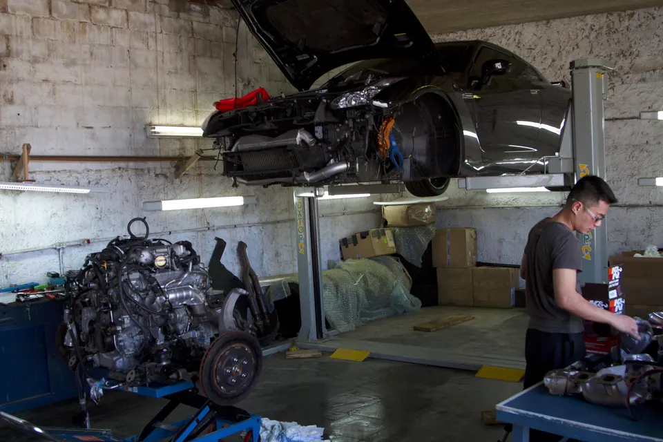 A Nissan GT-R on a lift in a performance shop with its engine removed, a mechanic working nearby.