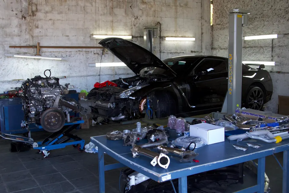 Black Nissan GT-R in a performance shop with its engine removed and various turbo and exhaust upgrade parts on a table.