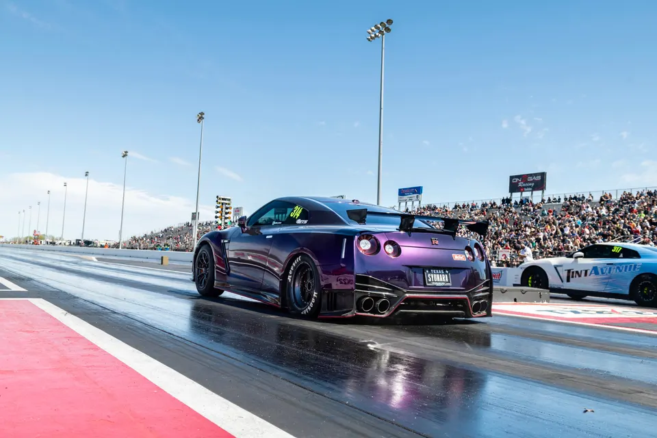 A purple Nissan GT-R with a widebody kit and large rear wing on a drag strip, preparing to race.