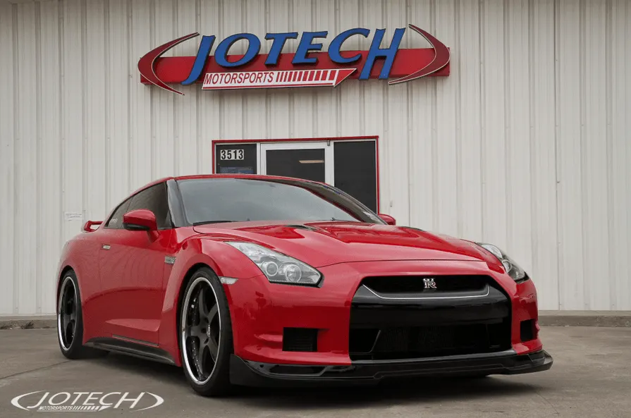 Red Nissan GT-R parked outside Jotech Motorsports performance shop with aftermarket wheels and front splitter.
