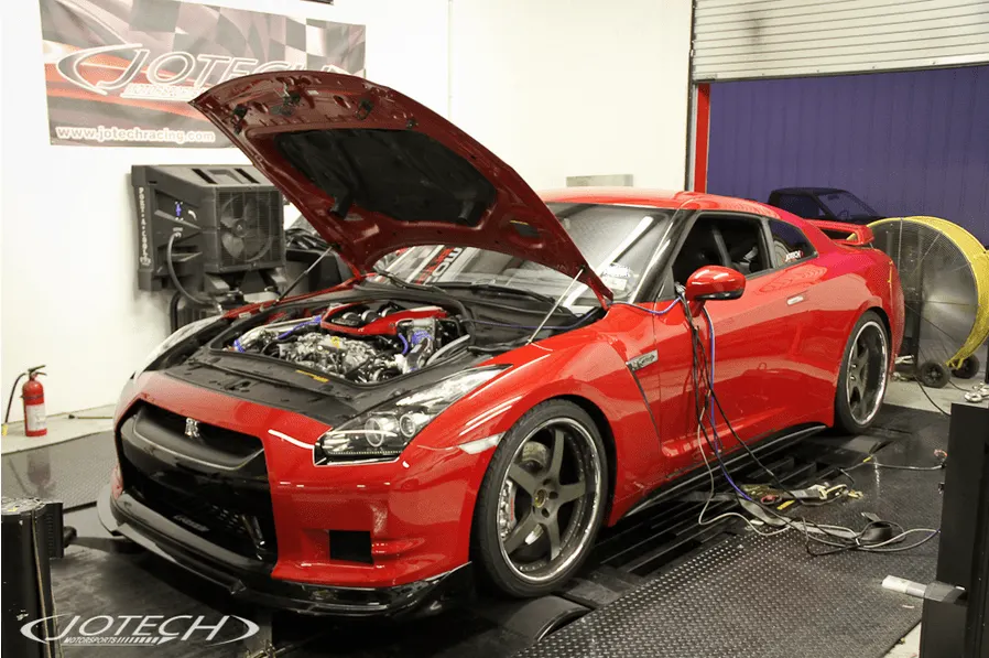 Red Nissan GT-R with its hood open on a Jotech Motorsports dynamometer, undergoing performance tuning.