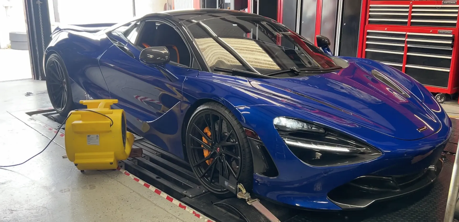 A blue McLaren 720S supercar strapped to a dynamometer for performance testing and tuning at a shop.