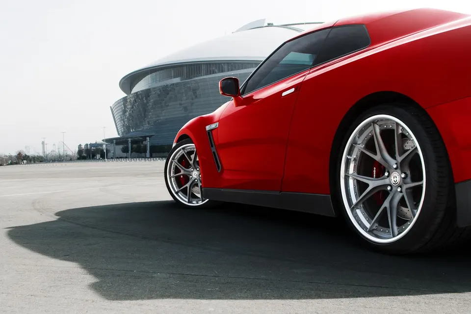 Red Nissan GT-R with custom aftermarket wheels and performance brakes parked in front of a modern stadium.