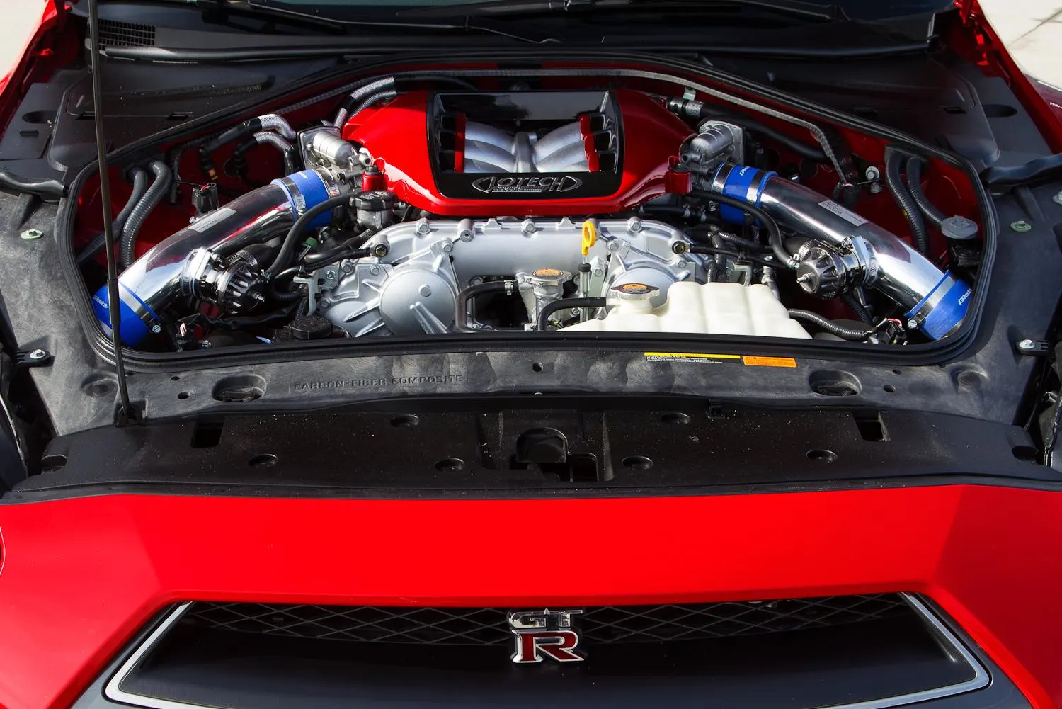 Close-up view of a Jotech-tuned Nissan GT-R VR38DETT engine bay with aftermarket chrome intake pipes and red engine cover.