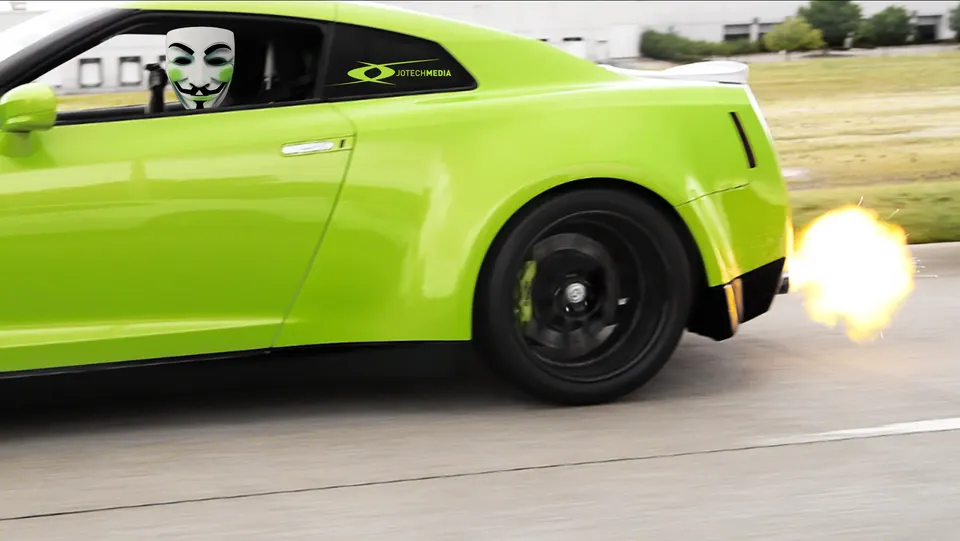 Green Nissan GT-R with an anonymous mask sticker on the window, shooting flames from the exhaust while driving.