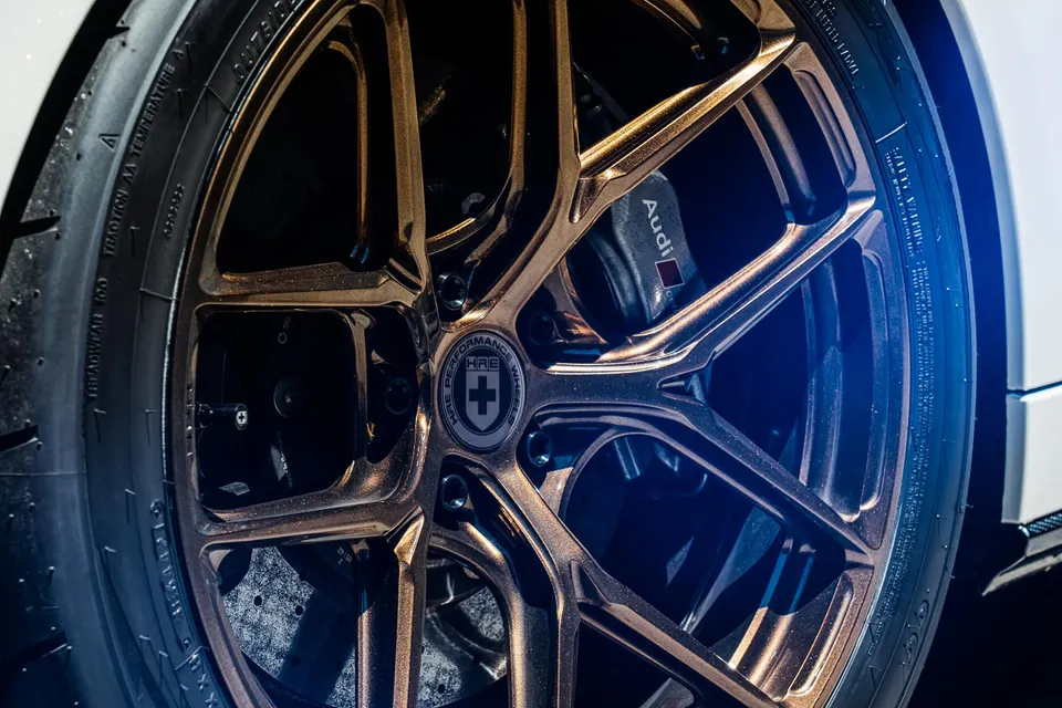 Close-up of a bronze HRE wheel with an Audi brake caliper and performance tire on a white car.